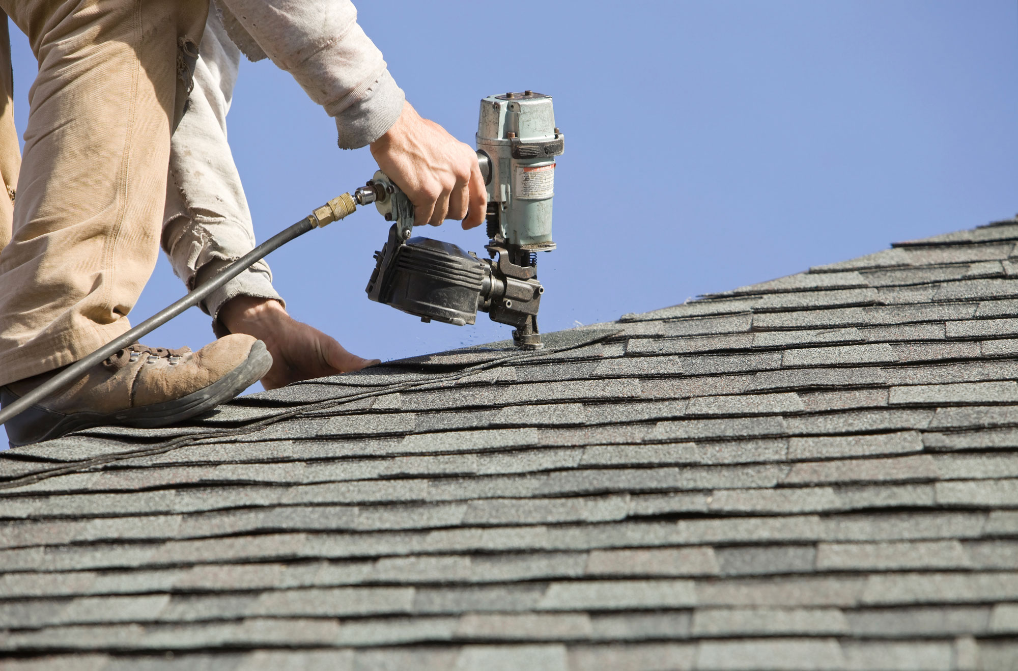 roofer using nail gun on new shingle roof 